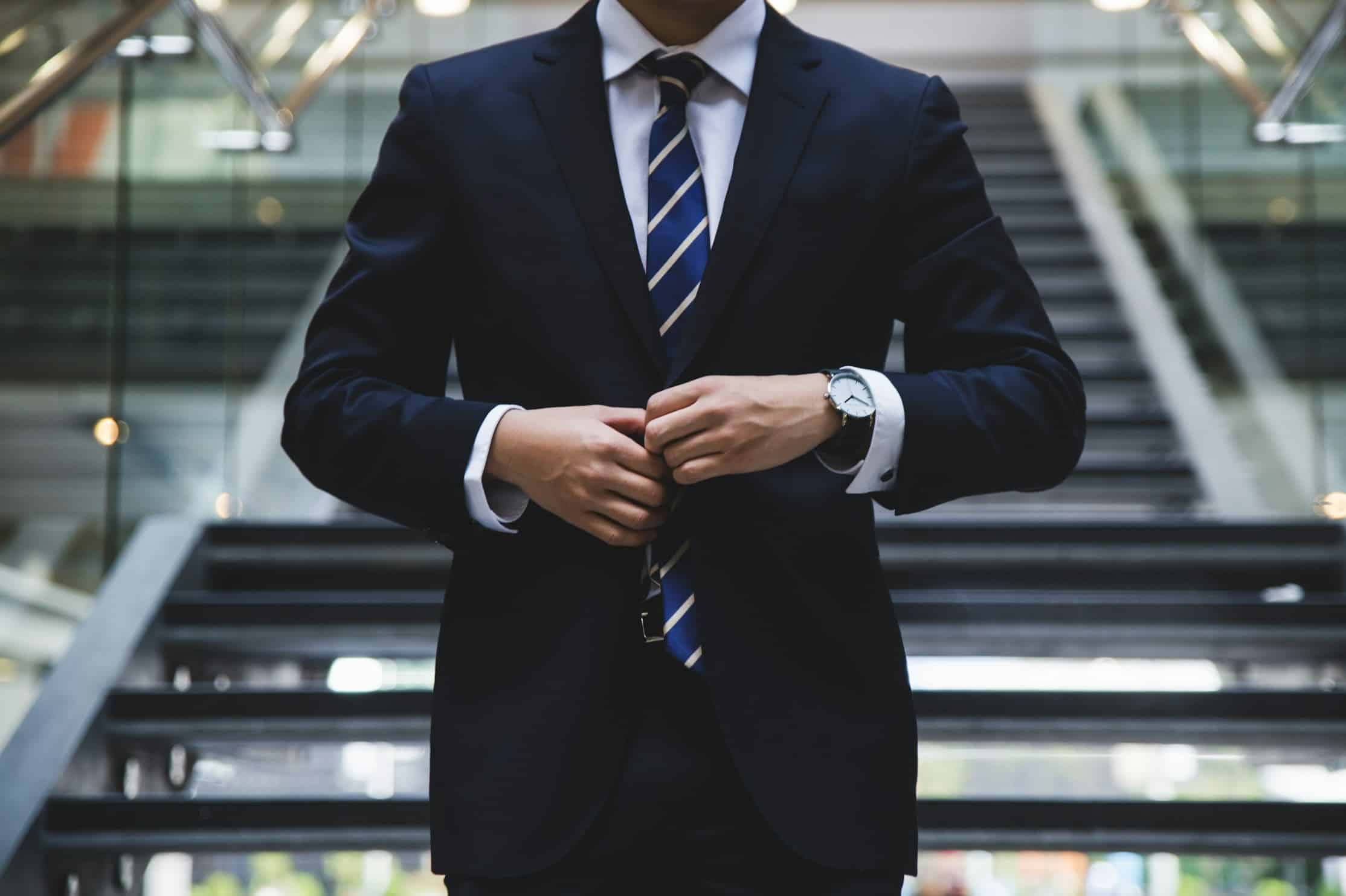 Neck down image of a man buttoning the blazer of his dark business suit.