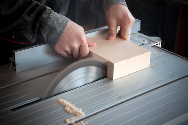 A woodworker uses a saw to cut down a small piece of wood.